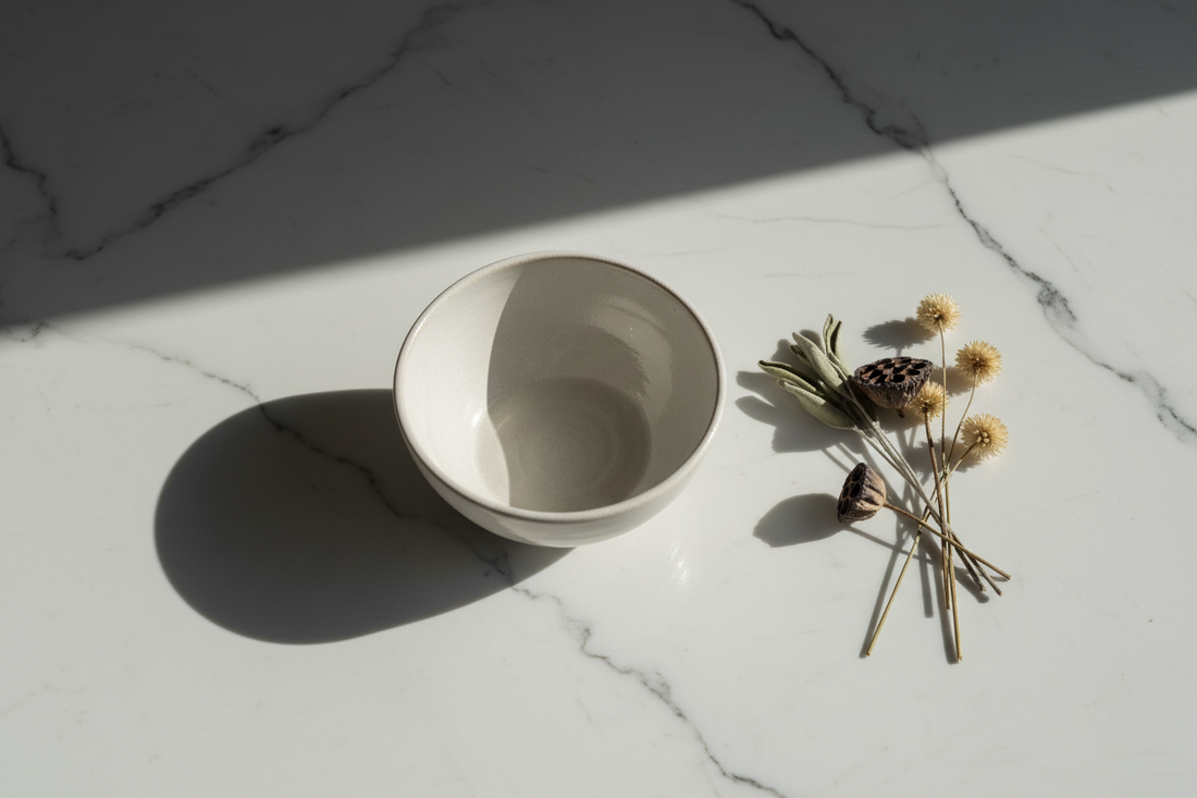 An empty ceramic bowl on white marble with soft morning light and dried botanicals — representing the stillness and intentionality of dry fasting